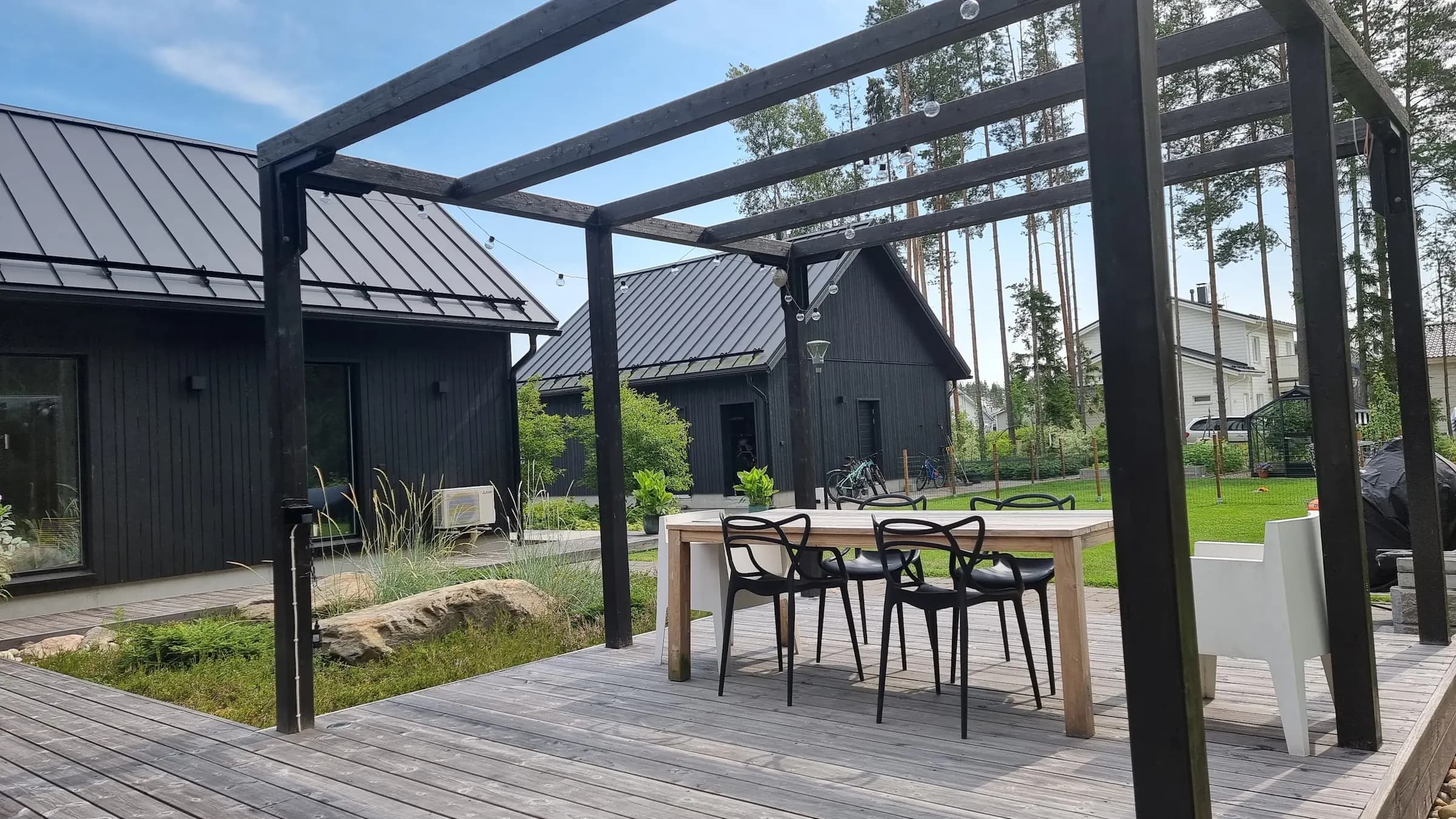 Ekologinen piha mustien latotalojen ja modernin pergolan ympärillä, Grand Design Pihatin suunnittelema
